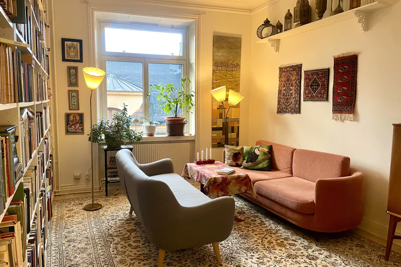 Vardagsrum med bokhyllor, orientaliska mattor och rosa soffa